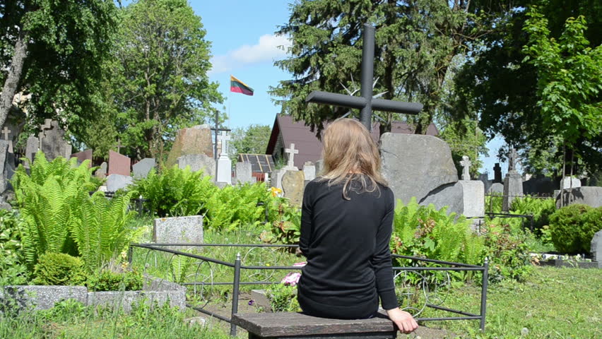 Sad young girl sit near boyfriend grave in cemetery. Patriot soldier died. National Lithuania flag.