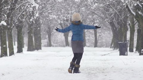 Slow Motion Total Shot Of Young Woman Spinning In Winter Tree Avenue. Her Arms Outstretched To Catch Falling Snowflakes.