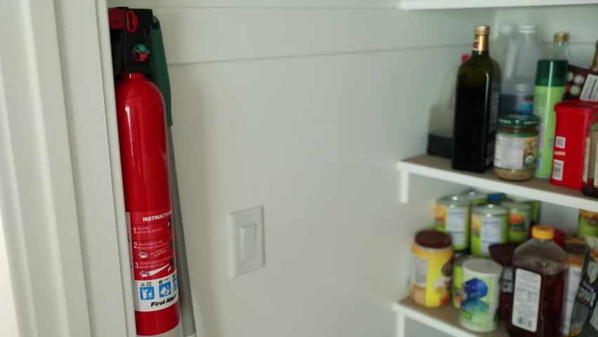 A man removes a fire extinguisher from the pantry and then puts in back