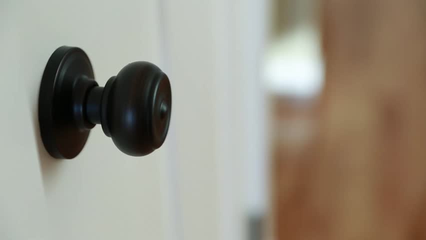 A hand twisting a door knob and opening a door