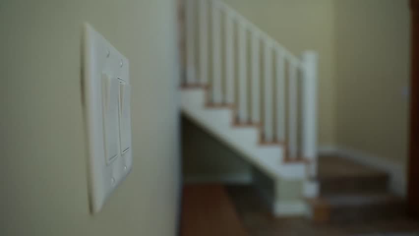 A man turns on a light switch and then walks upstairs in his home