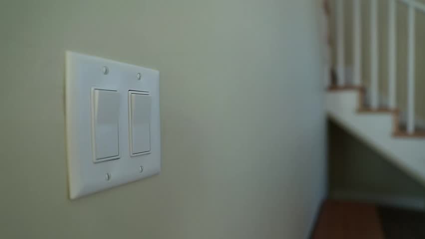 A hand turning on and off a light switch in a house