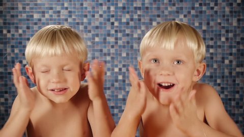 blond twin brothers using after shave cologne in bathroom
