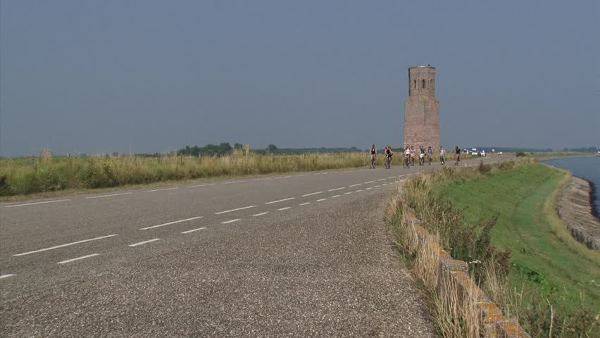 Cyclists passing Plompe Toren, a medieval tower at a dike along the Eastern Scheldt, The Netherlands. The tower is a remnant of a drowned village of Koudekerke, due to a flood in the 16th century.