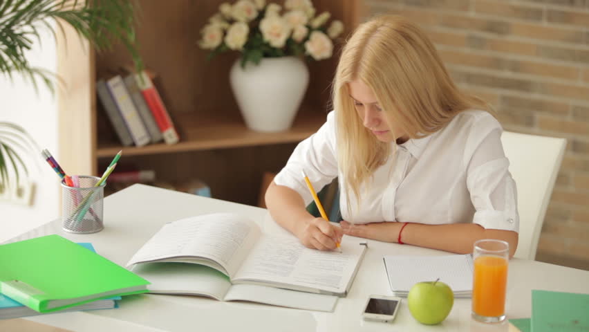 Blonde girl sitting at desk writing in notebook looking at camera and smiling