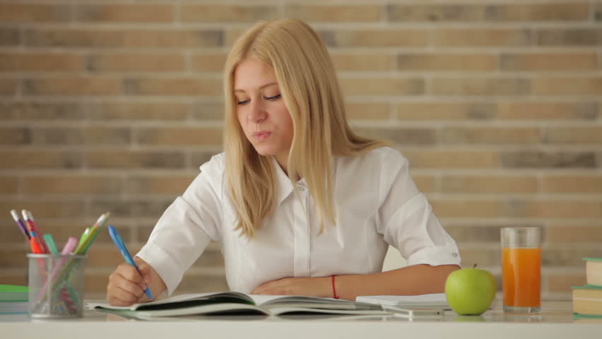 Charming girl sitting at desk studying writing in notebook drinking juice