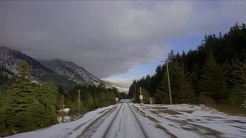 Point of view from train engine winding around western mountains with snow on ground, through tunnel
