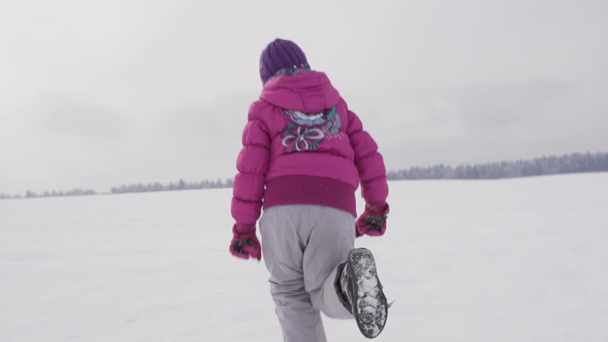 Slow Motion Rear View Of A Cute Girl Running Over Snow Covered Field. She Turns