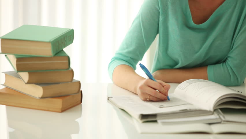 Cheerful girl sitting at desk writing in notebook looking at camera and smiling.