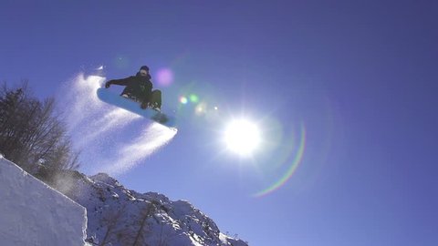 SLOW MOTION: Snowboarder jumps over kicker, low angle view