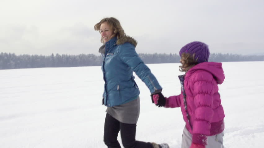 Slow Motion Of Mother And Daughter Holding Hands And Running Over Snow Covered