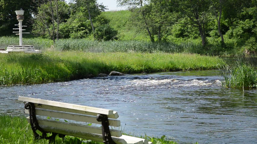 blonde young girl with a blue dress sits on an old white wooden bench by the stream