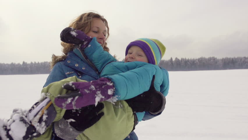Slow Motion Of Happy Mother Holding Her Son In Arms And Playing Outdoors In Snow