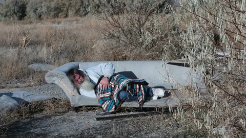 Man outdoor sofa homeless with blanket sleeping HD. Homeless man sleeps on discarded junk sofa near garbage dump. Homeless man long hair beard sad and poor. Sad and out of work needs help to survive.