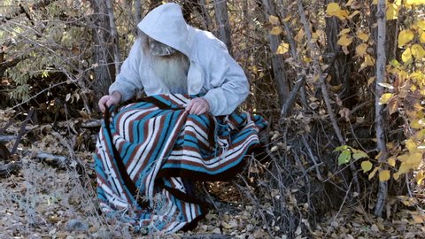 Homeless man sitting in trees with blanket HD. Long hair beard sad and poor. Down on luck, poor, hungry and depressed sits on tree stump along railroad tracks near urban city. Sad needs help.