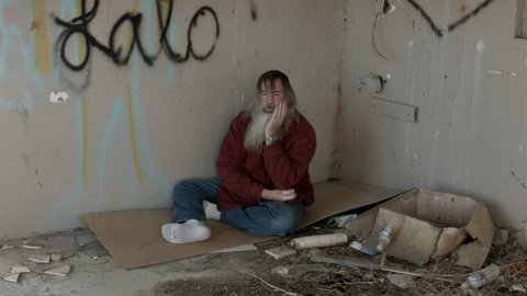 Abandoned building hopeless homeless man corner filth HD. Long hair beard sad poor sleeping. Down on luck, poor, hungry and depressed sits on discarded cardboard in urban city. Needs help to survive.