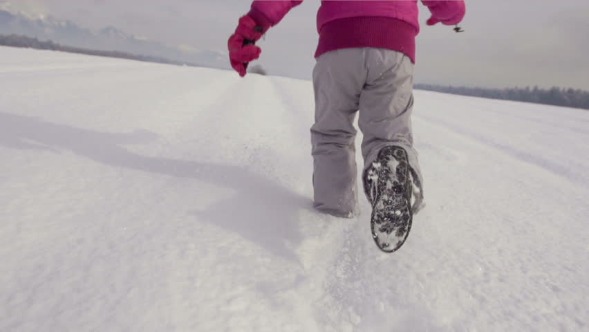Slow Motion Rear View Of A Girl's Legs Running Across Snow Covered Field On A
