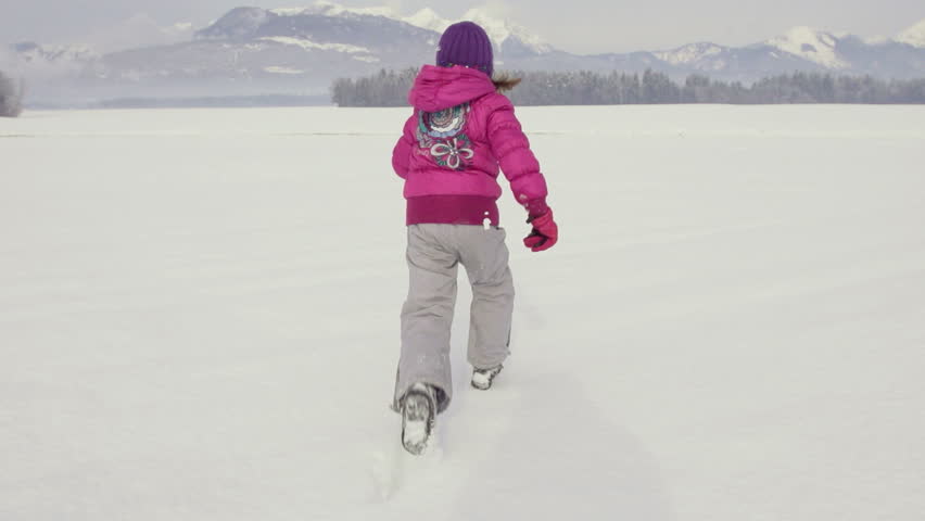 Slow Motion Rear View Of A Girl In Pink Parka Running Over Snow Covered Field