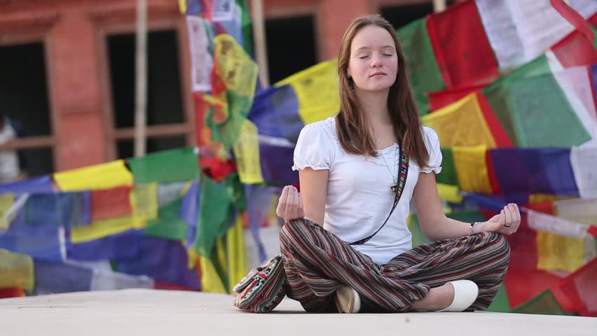 Young girl meditating in Lotos pose on the background of fluttering prayer flags