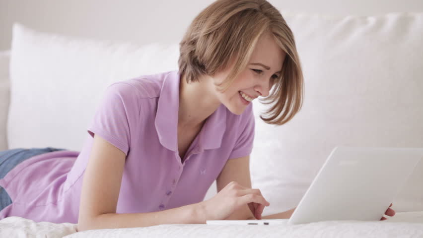 Charming girl relaxing on sofa using laptop looking at camera and smiling.