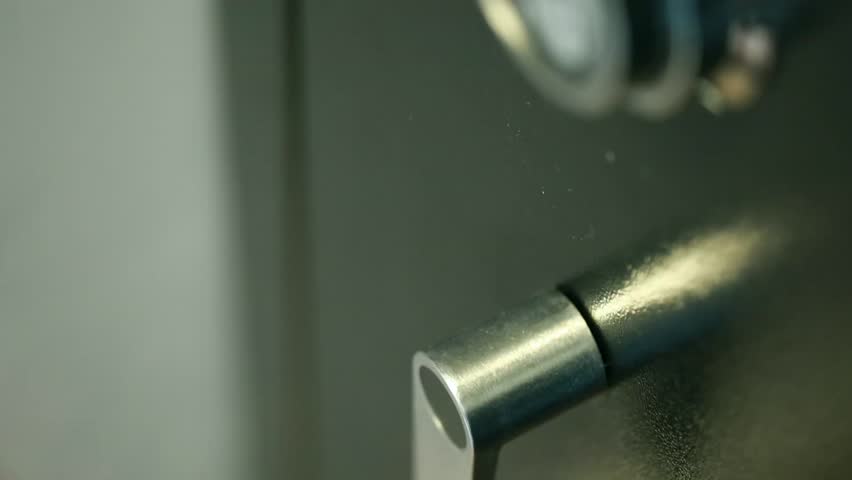 A hand opens a combination lock on a steel vault