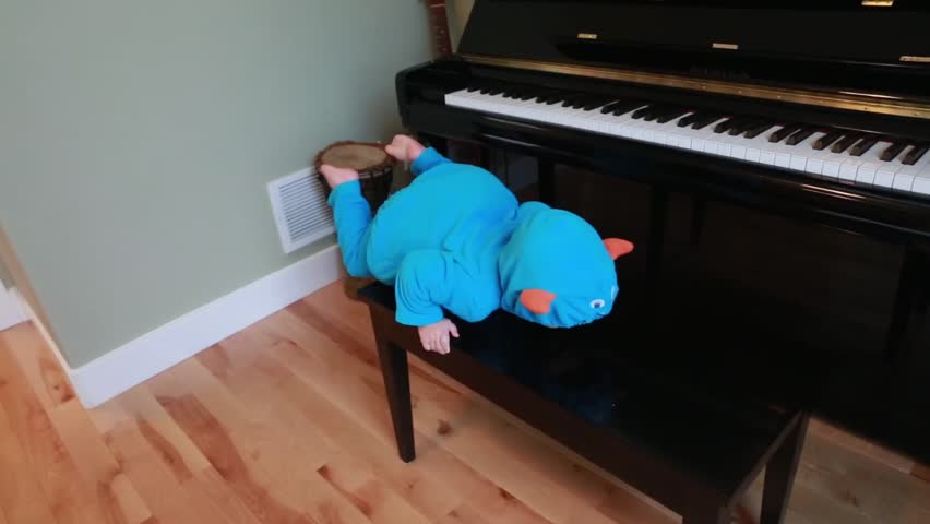 A toddler boy playing in a monster suit on a piano in his home