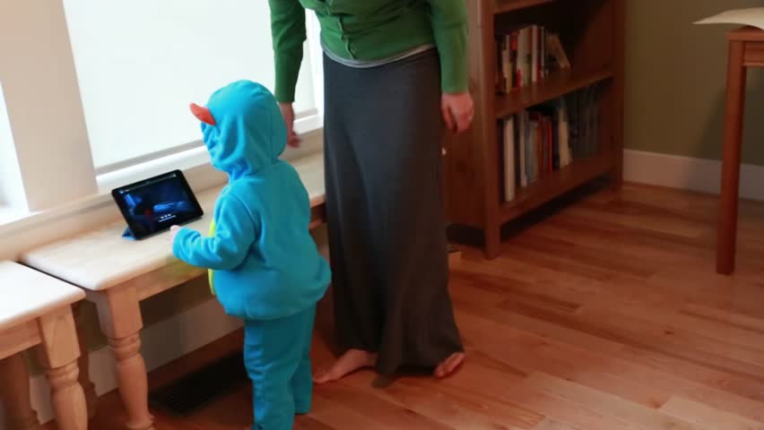 A working mother in a home office while her toddler plays in a monster outfit