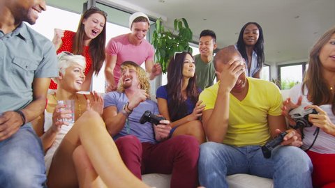 Happy mixed ethnicity group of friends socializing at home and enjoying the excitement of playing video games.  