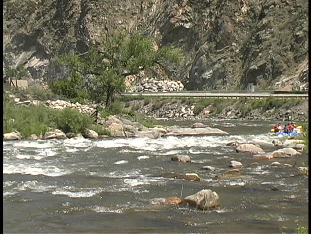 Camera zooms in and out and pans to follow rubber rafts as tourists  boat their way through a set of rapids on the Arkansas River of central Colorado