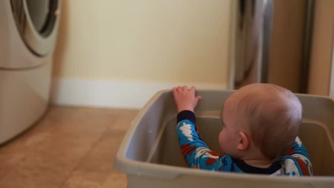 A boy falls over while playing in a laundry basket in his home