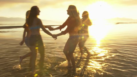 Group of Five Teenage Girls Dancing In The Water At The Beach At Sunset