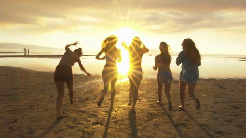 Group of Five Teenage Girls Run Into The Water, Celebrate On The Beach At Sunset