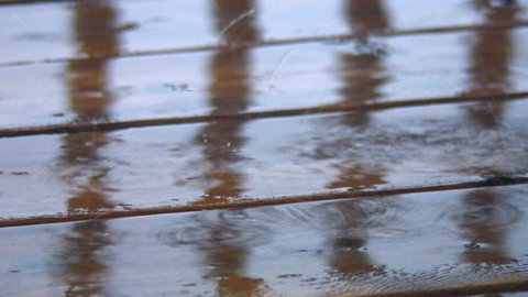 Close shot of water droplets splashing off wooden boards during rain storm. Good Audio.