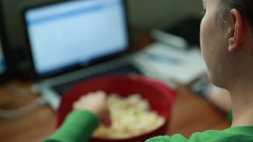 A woman working in her home office while snacking on popcorn