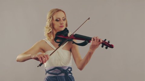 Young woman playing the violin on gray background