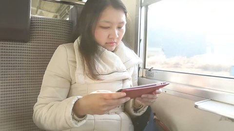 Asian woman using her tablet computer while traveling by train in autumn