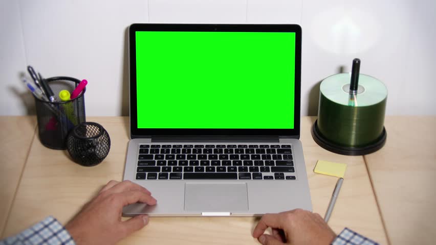 A man taps his fingers on his desk waiting for his laptop to operate. Green