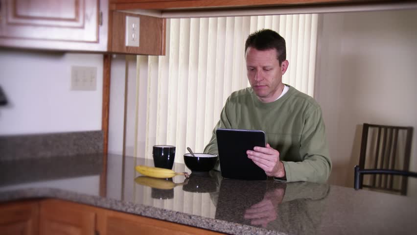 A man eats breakfast while looking at his tablet PC.