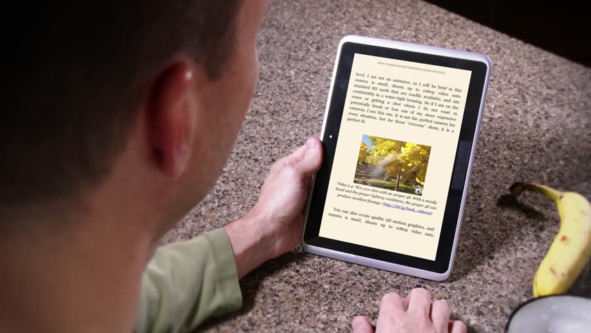 A man eats breakfast while reading an eBook on his tablet PC. eReader content