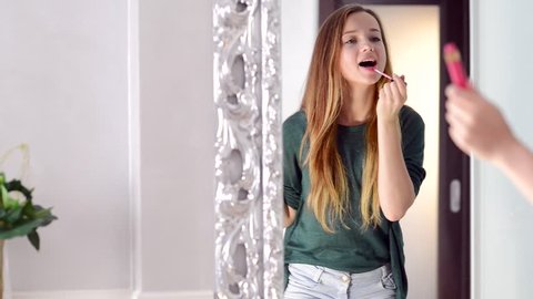 Beauty Teenage Girl applying Make up and admiring herself in the mirror. Beautiful Teenager Looking in the Mirror at home and putting makeup on. Teen Fashion