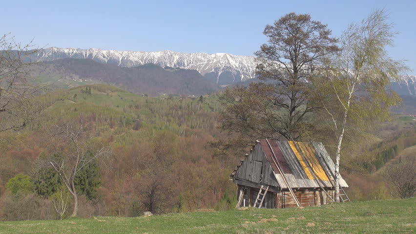 Mountain alp peak covered by snow and farm cottage on forest hill in spring day