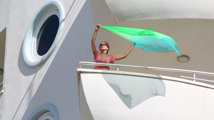 Girl waving kerchief on the balcony of the room at the hotel on the top floor