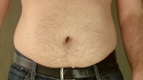 Overweight man shakes fat belly. Young Adult in jeans pants shakes his fat belly. Front shot.