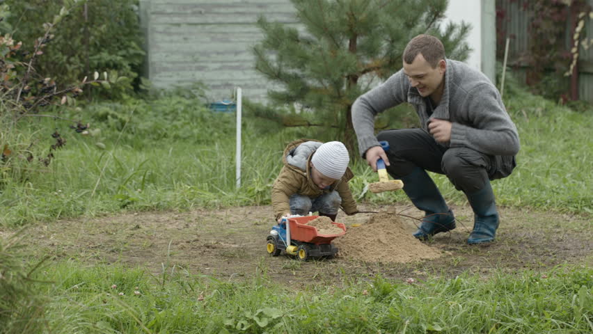 Father and son playing with toy truck loading it with sand. Family fun outdoors.