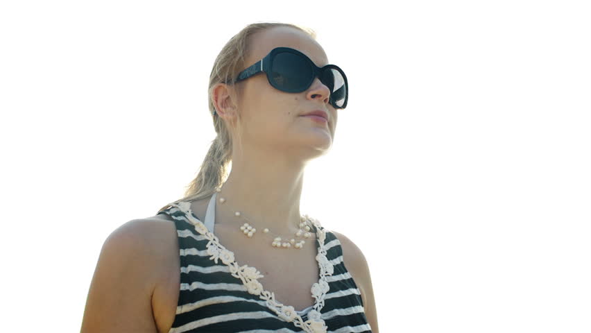 Happy young woman in sunglasses talking on the phone and sun shines behind her back.