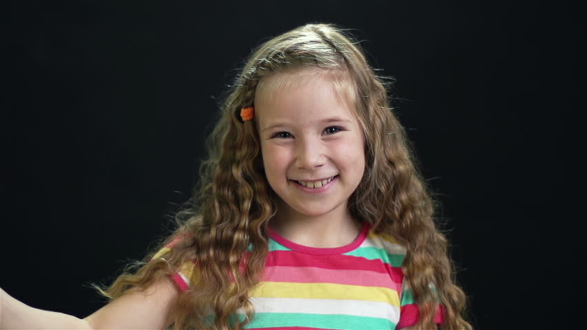 Slow-motion of a cheerful little girl with a sparkling Bengal light against dark background