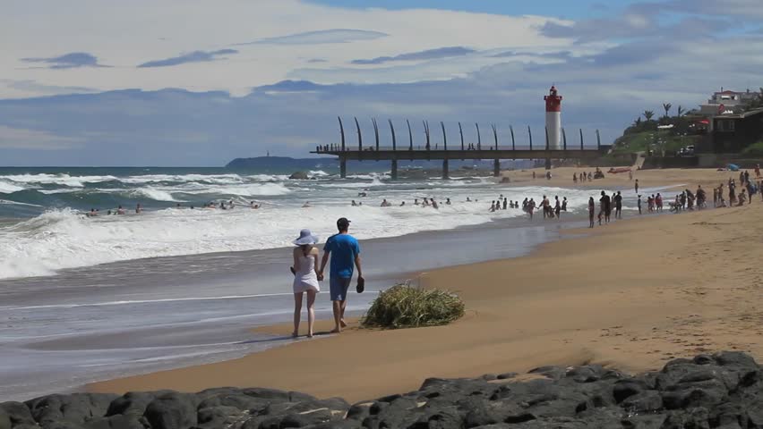 Couple walking on Umhlanga Rocks Beach with Promenade Pier and Lighthouse in the