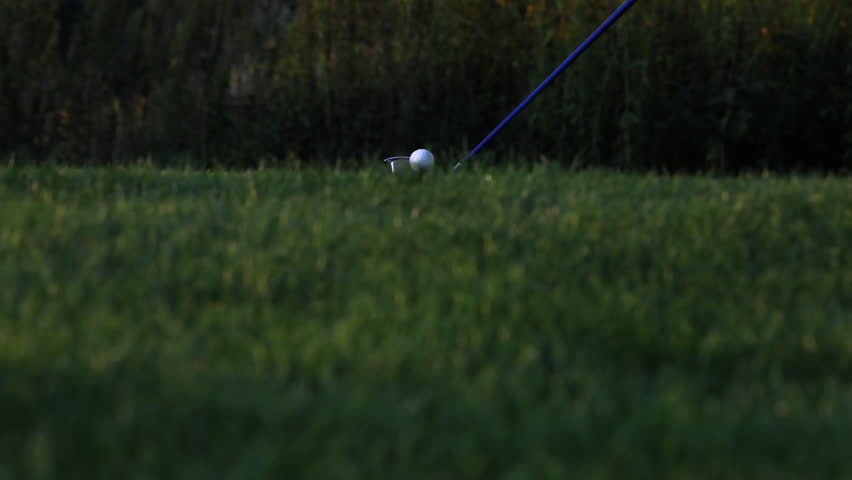 Close up of golf ball sitting on tee with driver swings and hits the ball