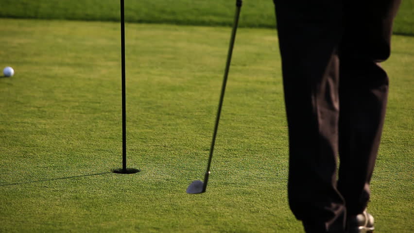 A golf player picking up golf balls lying around hole