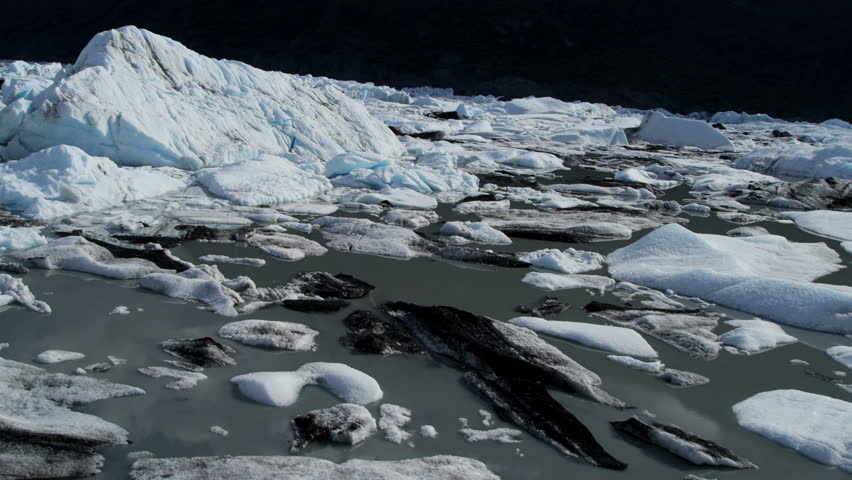 Aerial view broken off ice flows covered in moraine carried on the lake from the Knik Glacier northern end Chugach Mountains South Central Alaska, USA shot on RED EPIC. 4K, UHD, Ultra HD, resolution